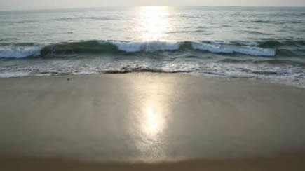 Imagen del océano visto desde la playa, con el Sol en frente, produciendo un fuerte reflejo de luz en el mar y en la arena húmeda.