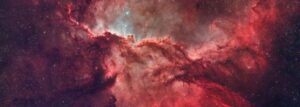 Descripción de imagen: fotografía de la parte central de la nebulosa, que se aprecia como una nube de gas y polvo, de color rojo con un poco de celeste en el centro, rodeada de zonas más oscuras, por efecto del mismo polvo. Se aprecian algunas estrellas, como puntos tenues en la imagen.